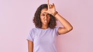 Menina fazendo um L (loser; em português: perdedor) na testa - AaronAmat/iStock