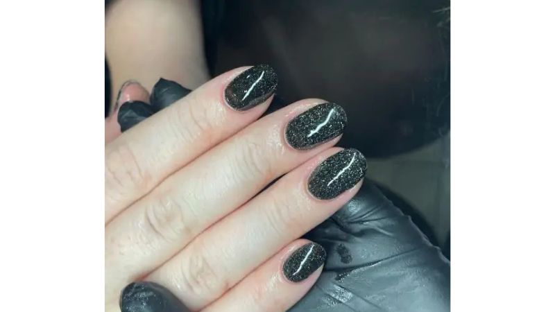 Unhas curtas também podem ser uma forma de expressão, ainda mais com unhas pretas com glitter.